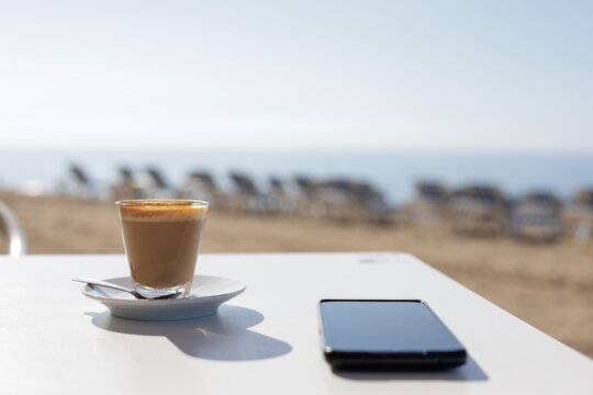 A cup of coffee and a mobile phone on a white table in a beach bar, without people. Workplace in a cafeteria in the morning of a self-employed person.