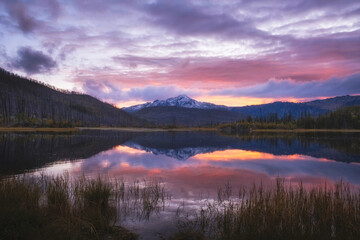 Beautiful autumn landscape during a colorful sunset with mountain lake Arashan where the peak with the first snow is reflected in the water in Kazakhstan. Altai Mountains in Katon Karagay Park.