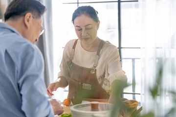 A woman prepares fresh vegetables in a cozy kitchen, while a man assists in the background. The scene emphasizes a warm and healthy lifestyle with a focus on fresh produce and home cooking.
