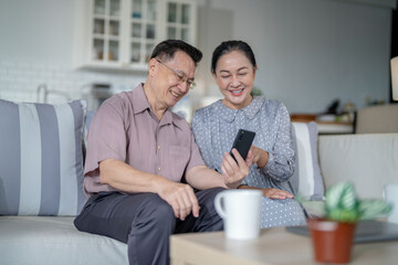 An elderly couple sits together in their cozy living room, smiling and enjoying a moment as they look at something on a smartphone. Their warmth and affection capture a peaceful home atmosphere.