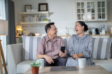 An elderly couple sits together in their cozy living room, smiling and enjoying a moment as they look at something on a smartphone. Their warmth and affection capture a peaceful home atmosphere.