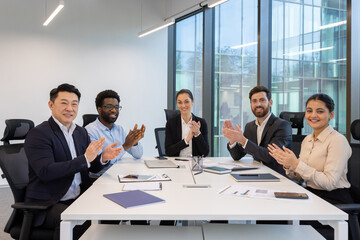 Positive business environment in office. Diverse group of professionals in meeting room clapping,...