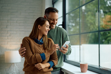 Happy couple using app on mobile phone by  window.