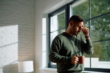 Distraught man with cup of tea by  window at home.