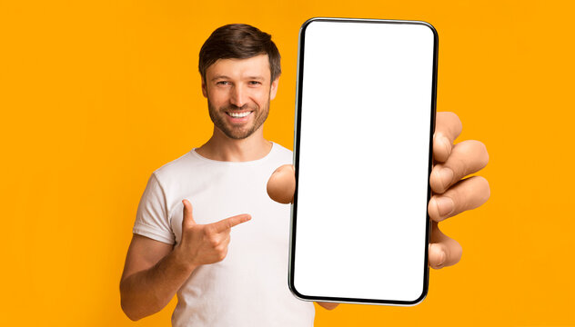 Recommendation. Portrait of excited bearded man holding big smartphone with white blank screen in hand, showing close to camera and pointing at device. Gadget with empty free space for mock up, banner