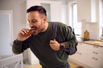 Hungry man taking  bite of food on his way out of  house.