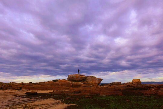 Paisaje de hombre subido a una roca bajo un cielo de nubes oscuras. 