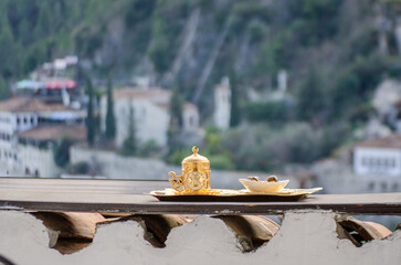 A traditional Turkish coffee set, made of gold and porcelain, rests on a wooden tray. The background is slightly blurred, creating a sens