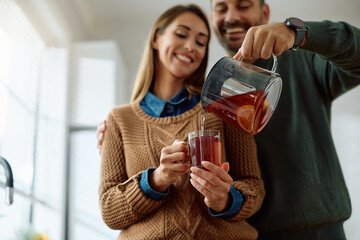 Close up of man pouring cup of tea to his wife at home.