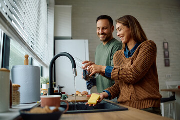 Happy couple cooperating while doing  dishes in  kitchen.