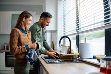 Happy couple washing dishes together in kitchen.