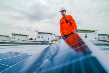 A worker in an orange safety jacket inspects solar panels on a rooftop, using a laptop to ensure...