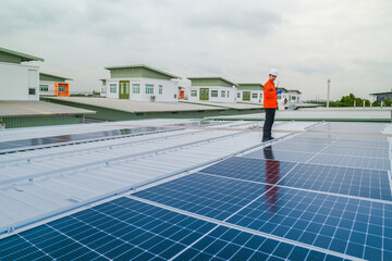 A worker in an orange safety jacket inspects solar panels on a rooftop, using a laptop to ensure...