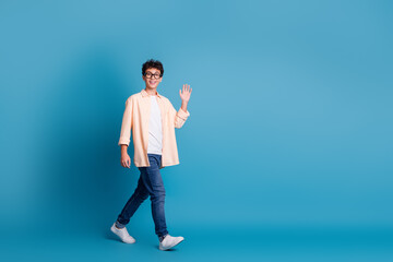 Joyful young man in casual attire against blue background waving, embodying modern youth and vibrant lifestyle