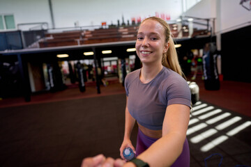 Young sporty woman getting a helping hand from a gym buddy to stand up after a workout session, smiling and showing camaraderie in the gym.