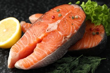 Fresh raw salmon steaks with spices, lemon, lettuce and dill on dark textured table, closeup