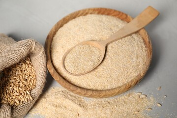 Oat bran in bowl, spoon and burlap bag with grains on grey table, closeup