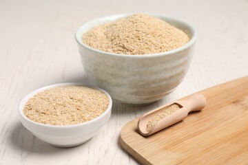 Oat bran in bowls and scoop on light wooden table, closeup