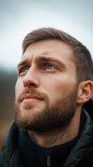Obraz premium A man with a beard gazes thoughtfully into the distance during a cloudy day in the countryside