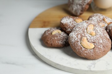 Tasty chocolate cookies with cashew and powdered sugar on white table, closeup. Space for text