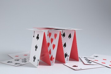 Collapsed house of playing cards on light grey background, closeup