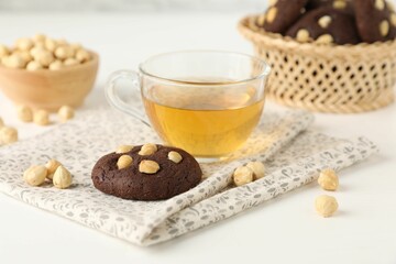 Tasty chocolate cookies with hazelnuts and tea on white table, closeup