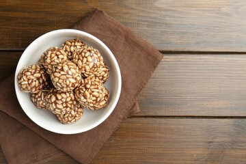 Tasty chocolate puffed rice balls in bowl on wooden table, top view. Space for text