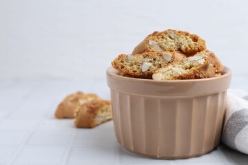 Tasty almond biscuits (Cantuccini) in bowl on white tiled table, closeup. Space for text