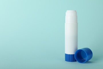 Glue stick and cap on light blue background, space for text