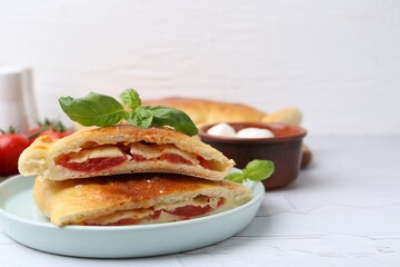 Pieces of tasty vegetarian calzone with tomato, cheese and basil on white textured table, closeup