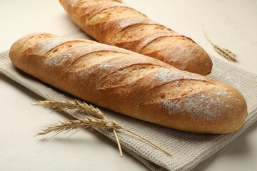 Fresh baguettes and spikes on beige table, closeup