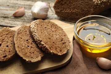 Slices of rye baguette, oil and garlic on wooden table, closeup