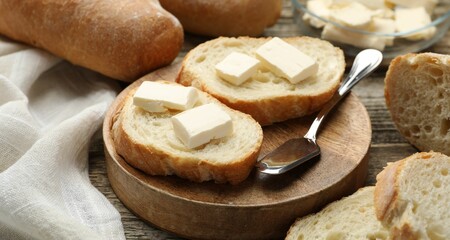 Slices of fresh baguette with butter on wooden table, closeup