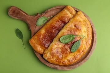 Tasty calzones with basil on green background, top view