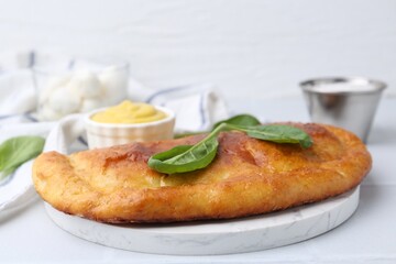 Tasty calzone with basil and sauce on white table, closeup