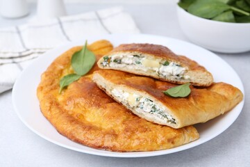 Tasty calzones with cheese and basil on light grey table, closeup