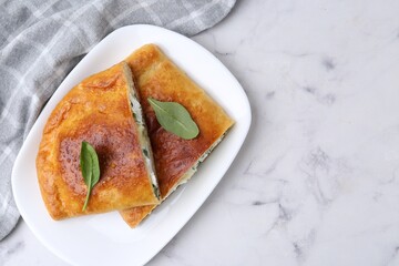 Pieces of tasty calzone with cheese and basil on white marble table, top view. Space for text