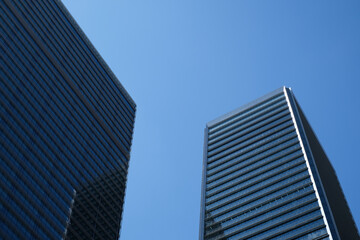 Obraz premium A low-angle view of two modern skyscrapers with glass facades under a clear blue sky, emphasizing contemporary architecture and urban development in a cityscape.