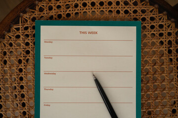 Flat lay weekly planner and a pen on a vintage rattan wicker chair. Flat lay, top view. Aesthetic copy space, mockup, template.