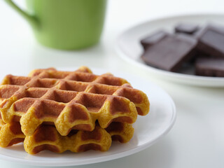Plates of homemade gluten free waffles and broken dark chocolate on a table near a mug. Close up.