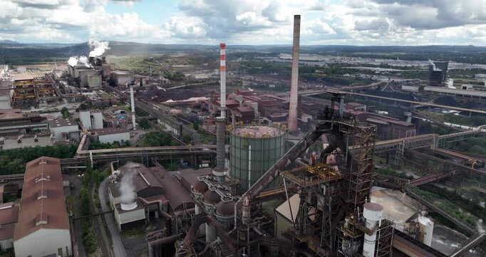 Drone footage of steel fabrication factory with blast furnace and smoke coming out of chimneys.