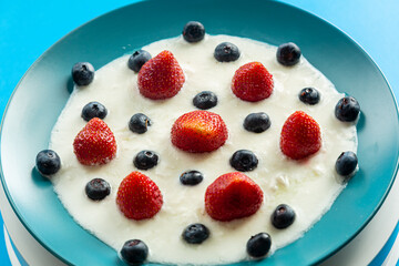 Fresh berries strawberries and blueberries in a blue plate with whipped cream on a blue background