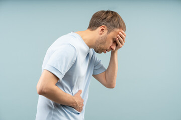 Weary crouched man holds forehead, stomach struggling with dizziness, nausea feels symptoms of high blood pressure by stress, fatigue, food poisoning dehydration. Cardiovascular problems, hypertension