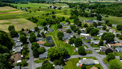 Aerial view of a tranquil rural community featuring various Mobile, Prefab, Manufactured houses situated near lush green fields and trees. The landscape shows harmonious blend of residences farmland.