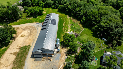 A large agricultural building with solar panels is being constructed in a rural setting. The site is surrounded by greenery and features open land, indicating future agricultural use.