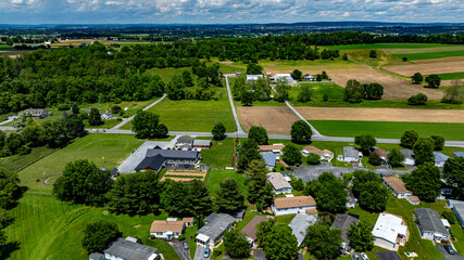 Aerial view of a tranquil rural community featuring various Mobile, Prefab, Manufactured houses situated near lush green fields and trees. The landscape shows harmonious blend of residences farmland.