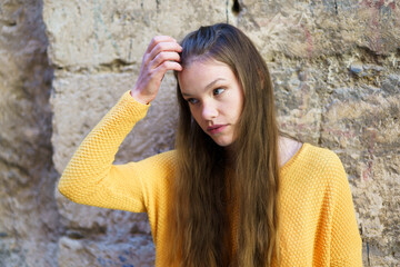 A Thoughtful Young Woman Dressed in a Bright Yellow Sweater Posing Against a Stone Wall