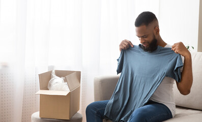 African american man tries on a tshirt received from online store, copy space