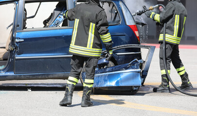 firefighters wearing fire resistant suits and amphibious boots during a car fire extinguishing intervention with a torn off door