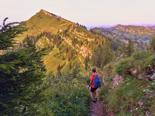 pretty senior woman hiking in warm dawn sunlight and enjoying the spectacular view over the Allgau...